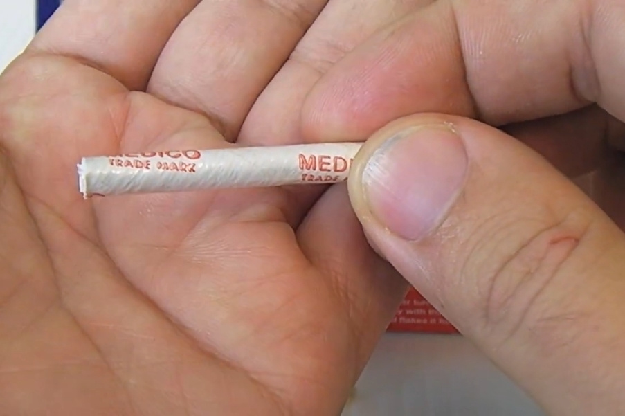 Primo piano di una mano che tiene un filtro per pipa Medico con testo rosso su carta bianca.